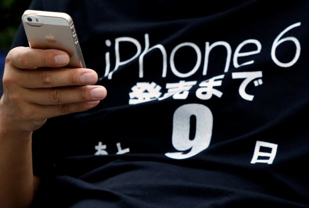 A man uses his iPhone 5 as he camps, ahead of the September 19 release of iPhone 6 and iPhone 6 Plus, in front of an Apple Store at Tokyo's Ginza shopping district