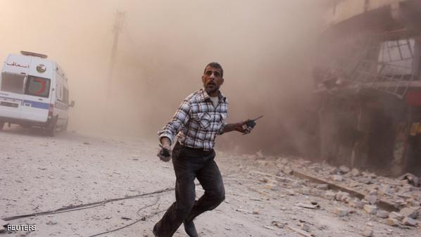 A man holding walkie-talkies runs towards a site damaged by what activists said were barrel bombs dropped by warplanes loyal to Syria's President Assad, in Aleppo