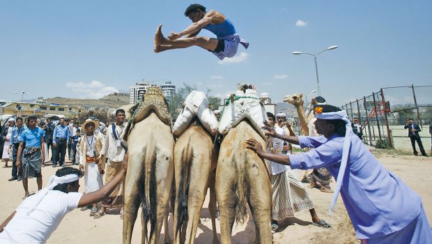 A Bedouin man jumps over camels during the Sanaa Summer Festival in Sanaa