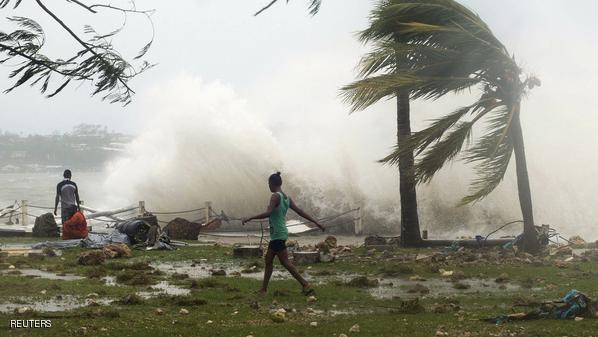 Local residents walk past debris as a wave breaks nearby in Port Vila, the capital city of the Pacific island nation of Vanuatu